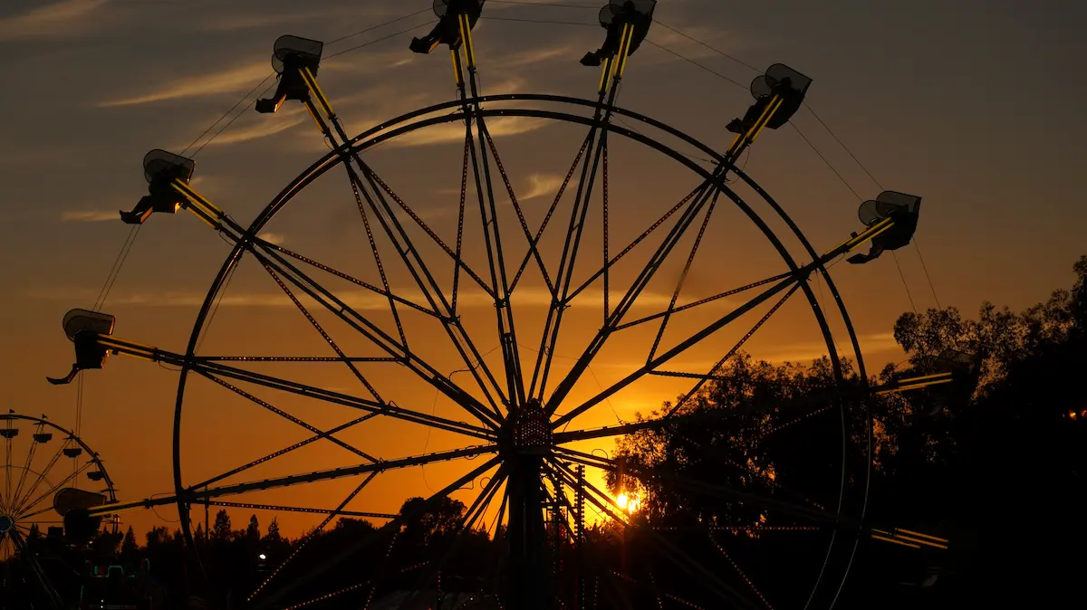 Silhouetted ferris wheel at sunset with glowing orange sky symbolizing perspective lifes emotional ups and downs reflection and finding balance and hope through the healing journey in therapy
