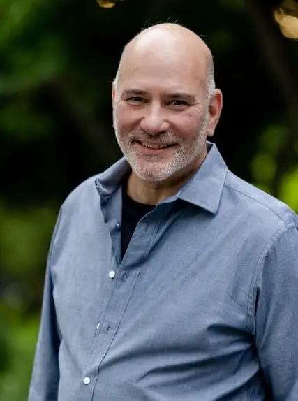 Smiling dr adam klein wearing a blue button down shirt outdoors against a blurred green background